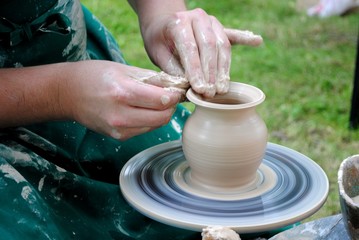 Potter's hands guiding child's hands to help him to work with the pottery wheel