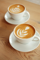 Two white cups of fragrant cappuccino stand on a wooden table. Coffee with milk  on the table, top view.