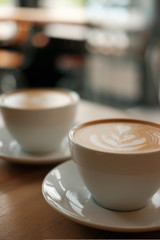 Two white cups of fragrant cappuccino stand on a wooden table. Coffee with milk  on the table,...