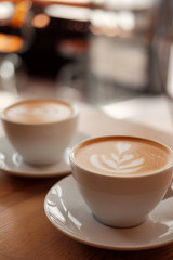 Two white cups of fragrant cappuccino stand on a wooden table. Coffee with milk  on the table, front view.