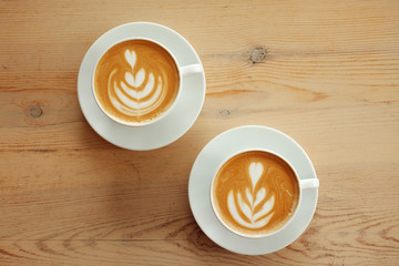 Two white cups of fragrant cappuccino stand on a wooden table. Coffee with milk  on the table, top view.