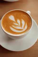 White cup of fragrant cappuccino stand on a wooden table. Coffee with milk  on the table, front view.