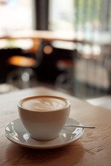 White cup of fragrant cappuccino stand on a wooden table. Coffee with milk  on the table, front view.