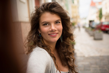 Obraz premium Young tourist woman doing selfie, showing positive emotions. Happy traveler on sidewalk, taking selfie pictures.