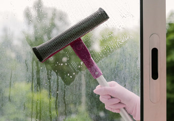 Hand in protective glove washing and cleaning window with professionally squeegee