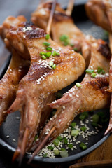 Close-up of roasted chicken wings on wooden skewers with sesame and green onion, selective focus