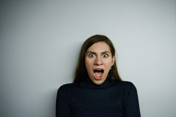 Shocked hysterical young Caucasian woman in black turtleneck sweater shouting, staring at camera with despair and terror, feeling panic while being late for plane, exam or some important event