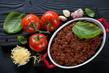 Bowl with bolognese sauce, green basil, fresh red tomatoes, garlic and parmesan cheese, top view