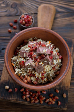 Pilaf with beef meat and pomegranate served in a ceramic bowl, elevated view on a rustic wooden background, vertical shot