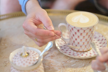 Hand of a young man with a spoon over a cup of coffee cappuccino on a table in a cafe
