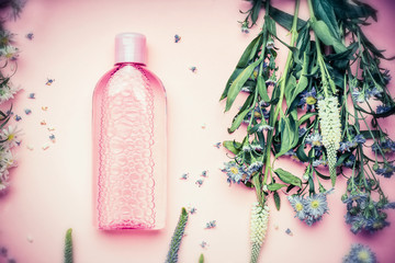 Plastic bottle with tonic or micellar cleansing water with fresh herbs and flowers on pink...