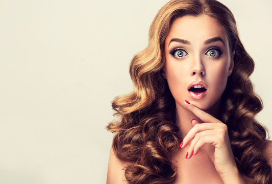 Shocked and surprised girl  presenting  your product . Curly hair woman amazed .Beautiful girl  with curly hair and red nails manicure. Expressive facial expressions
