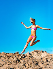 Photo of beautiful young model jumping, in the air, on pile of sand and blue sky background. Vertical view