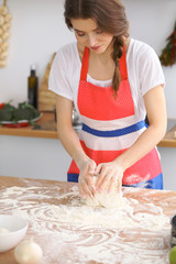 Young brunette woman cooking pizza or handmade pasta in the kitchen. Housewife preparing dough on wooden table