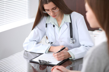 Female doctor having a talk with her patient  while sitting at the table near the window in hospital. Physician is ready to help patient. Medicine and health care concept