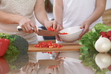 Close-up of four human hands are cooking in a kitchen. Friends having fun while preparing fresh salad. Vegetarian, healthy meal and friendship concept