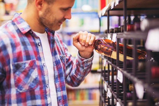 Young man choosing and buying wine in supermarket