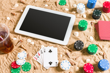 Fototapeta na wymiar Online poker game on the beach with digital tablet and stacks of chips. Top view