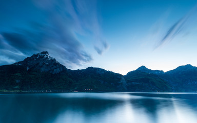 After sunset on the tops of the mountains. Evening clouds over the mountains. Long exposure. Reflections in the surface of the lake.