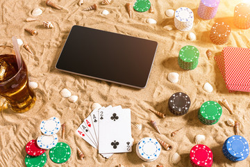 Online poker game on the beach with digital tablet and stacks of chips. Top view