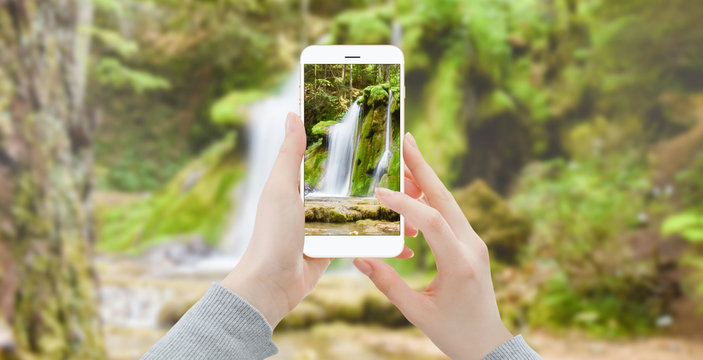 Woman with smartphone in the woods taking photo of waterfall