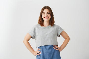 Naklejka premium Portrait of young happy beautiful girl smiling looking at camera with arms akimbo over white background.