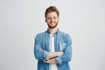Portrait of young handsome man in jean shirt smiling looking at camera with crossed arms over white...