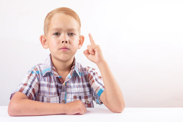the boy sits at the table , and held up the index finger of the concept of learning to follow the rules, the idea of obrazovania
