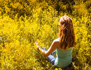 Naklejka na ściany i meble Lady is engaged in meditation in a city Park among yellow flowers. Beautiful woman doing yoga meditation in park. 