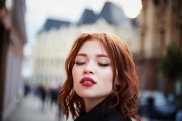 Fototapeta premium Portrait of a beautiful redhead. Fiery hair and full lips. Walking around the city