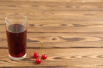 Cherries juice in glass on old wooden background