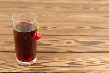Cherries juice in glass on old wooden background