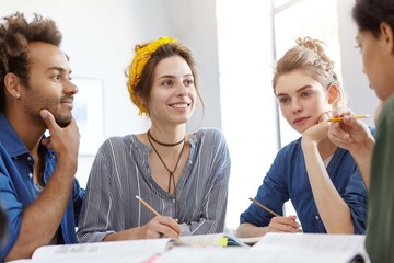 Three female and thier Afro American friend sitting togehter discussing something writing notes looking at each other. Mixed race creative workers working at their project work sitting indoors