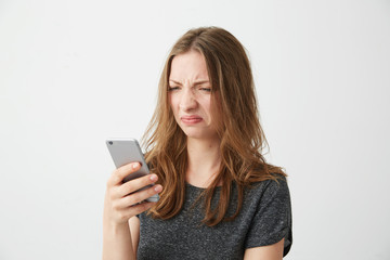 Displeased dissatisfied young girl looking at phone screen over white background.