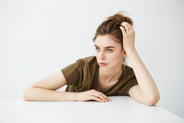 Bored tired dull young girl student with bun sitting at table over white background.