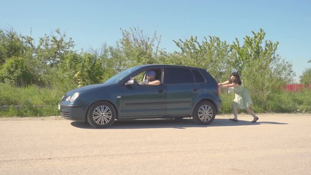 Young woman  in green dress pushing a car while man is emboldening her.Transportation, teamwork, funny concept