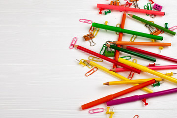 Colorful pencils and felt-tip pens, paper clips, stationery nails, smilie binders on white wooden...
