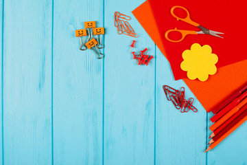 Red and orange pencils, felt-tip pens, notepaper, paper clips, stationery nails, felt and scissors on blue wooden background