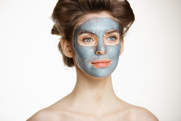 Beautiful tender naked girl in hair curlers and facial mask smiling over white background. Beauty health cosmetology and skincare.