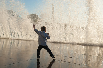 playful little kid playing with giant waves at ocean sunset