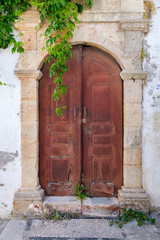 Fototapeta na wymiar Very old wooden door in traditional carved stone door-frame. Village of Lindos, Rhodes, Greece.