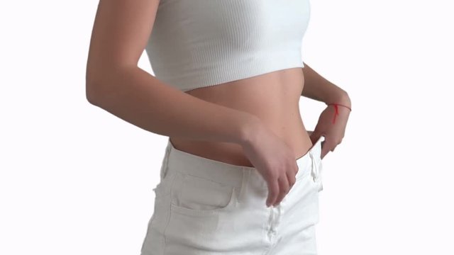 The girl shows that she has lost weight and pants at the waist are wide, on the White background