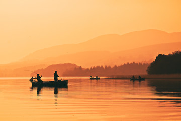 Man fishing on lake from boat at sunset. Lake of Menteith, Stirlingshire, Scotland, UK - Powered by Adobe