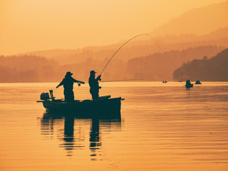 Silhouette of man fishing on lake from boat at sunset. Lake of Menteith, Stirlingshire, Scotland, UK - Powered by Adobe