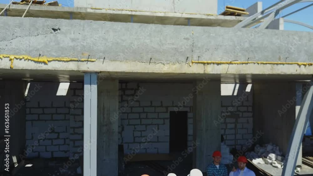 Poster aerial shot of builders team on construction site discussing plan of project with architect and cont