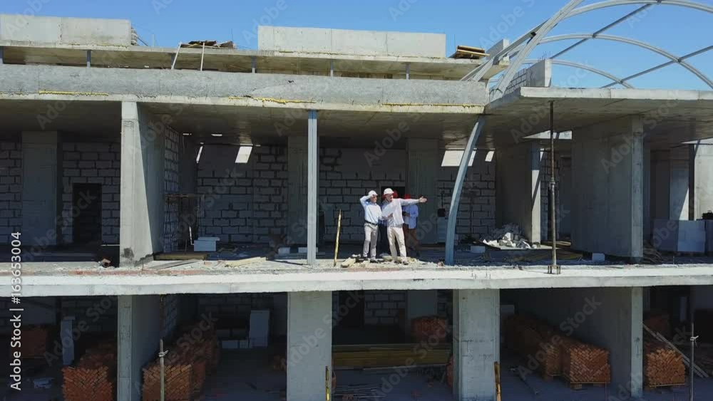 Poster aerial shot of builders team on construction site discussing plan of project with architect and cont
