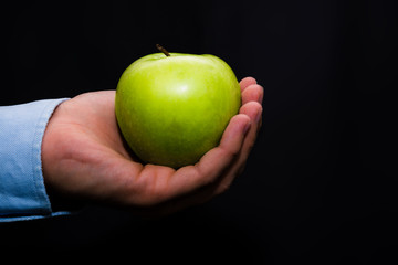 Zielone jabłko trzymane w ręce na ciemne czarne tło