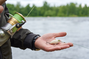 Wobbler in man’s hand and spinning rod reel against rapid river.