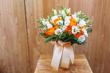 Wedding bouquet on shabby wooden background. Bride's traditional symbolic accessory. Floral composition with eustoma (or Lisianthus) and orange roses.