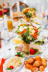 Fototapeta na wymiar Table set for wedding banquet with cutlery. Floral decorative elements - vases with bouquets of orange roses and white eustoma (or Lisianthus) flowers.